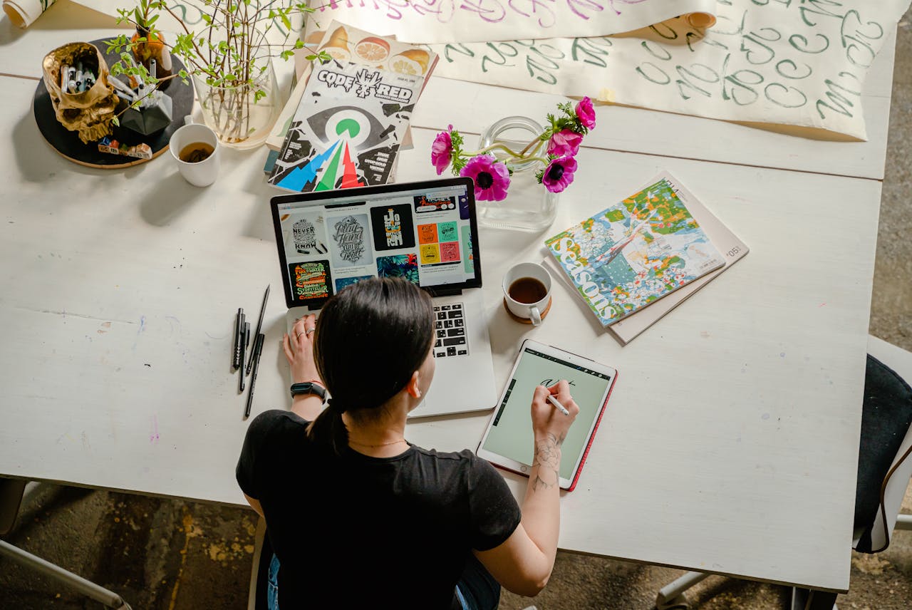 who-we-are Artistic workspace featuring calligraphy and digital design on a tablet and laptop.